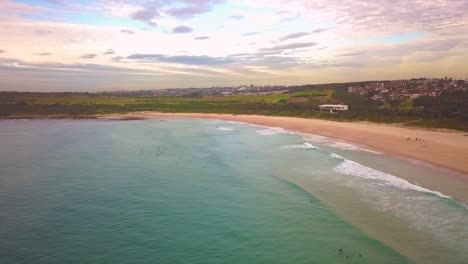 Aerial-shot-of-surfers-catching-waves,-surfing-in-winter-on-a-windy-cloudy-morning,-Maroubra-Beach,-Sydney-Australia