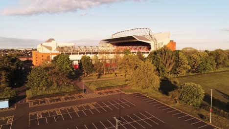 Das-Ikonische-Stadion-Des-Anfield-Liverpool-Football-Club-Bei-Sonnenaufgang,-Luftaufnahme-Beim-Abstieg-Zum-Leeren-Parkplatz