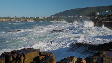 Panning-shot-of-waves-crashing-violently-into-rocky-coastline-of-Hermanus,-South-Africa