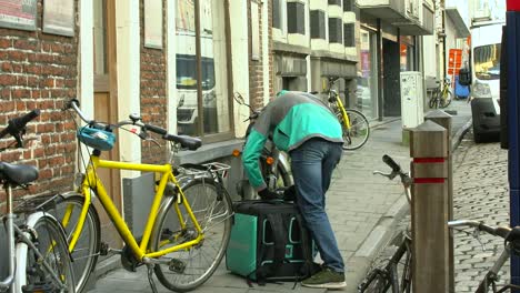 Deliveroo-Courier-Opens-The-Bag-Of-Food-Delivery-Outside-A-Building-In-Ghent,-Belgium---wide-shot