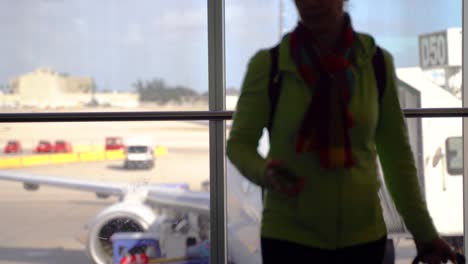Silhouette-of-woman-putting-her-phone-away-and-rolling-out-of-the-frame-with-blurry-airplane-in-distance-at-the-boarding-gate