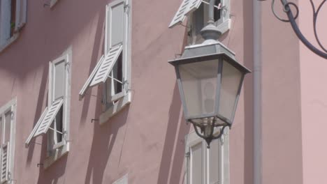 Close-up-slowmotion-shot-of-an-old-lantnern-lamp-in-an-alleyway-in-Riva-Del-Garda-with-a-rosa-building-in-the-background