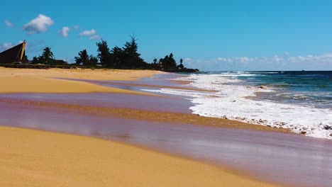 HD-Hawaii-Kauai-slow-motion-low-trucking-shot-of-ocean-on-right-and-waves-coming-in-from-right-to-left-with-beach-on-left-and-trees-in-distance-with-mostly-blue-sky