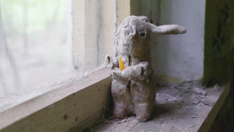 Torn-Bunny-Stuffed-Toy-Standing-By-The-Glass-Window-In-The-Exclusion-Zone-Of-Abandoned-Kindergarten-In-Pripyat-Near-Chernobyl,-Ukraine---Closeup-shot