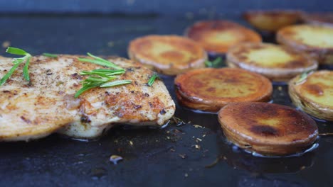 Grill-pan-full-of-sliced-potatoes-with-chicken-meat-steak,-side-closeup-view