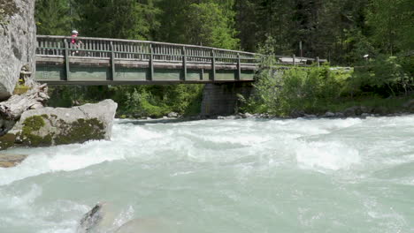 Bridge-over-big-stream-in-the-woods-of-italian-Alps-slow-motion-100-fps
