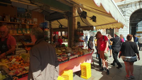 Slow-dolly-shot-of-tourists-visiting-traditional-italian-market-stall-with-fresh-fruits-and-vegetables-during-hot-day-in-Venice