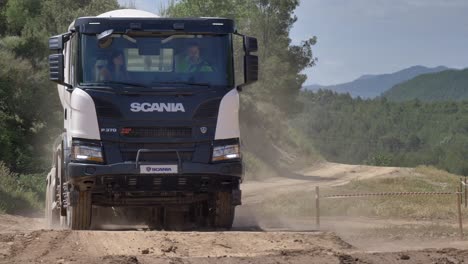 Camión-Scania-Pasando-Por-Un-Curso-De-Prueba-En-Una-Pista-De-Tierra-Polvorienta-Con-Un-Entrenador-A-Bordo