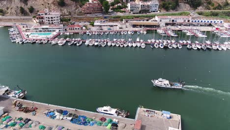 Aerial-view-of-a-boat-entering-the-calm-harbour-of-Arenys-de-Mar-near-Barcelona,-Spain