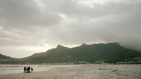 Gesperrte-Aufnahme-Eines-Leeren-Strandes-An-Der-Hout-Bay-In-Südafrika-Am-Abend-Mit-Bewölktem-Himmel-Und-Dunstigen-Bergen-Im-Hintergrund