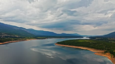 aerial-camera-flying-sideways-on-a-wide-shot-of-a-beautiful-mountain-scenery-on-a-cloudy-day,-with-nice-reflections-in-a-lake