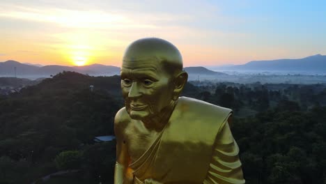 4k-Aerial-Close-up-shot-of-a-Biggest-Luang-Pu-Thuat-statue-in-the-world-surrounded-by-mountains-of-Khao-Yai-at-dawn-in-Thailand