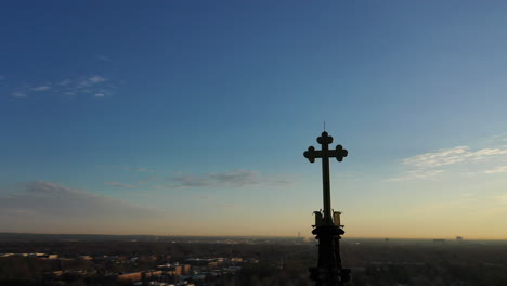 An-aerial-shot-of-a-cathedral's-steeple-with-a-cross-on-it-during-at-sunrise