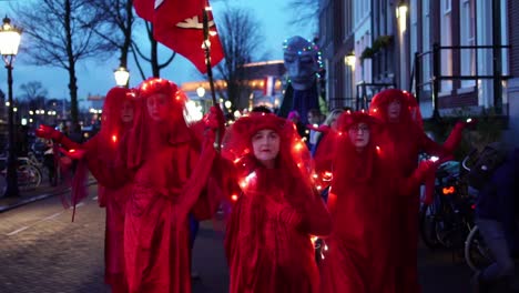 Red-Rebels-Parade-In-Amsterdam,-Netherlands-At-Dusk---Extinction-Rebellion-Activists-Wearing-Red-Dress-With-Lights---slow-motion
