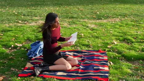 A-female-college-student-reading-a-book-and-relaxing-outdoors-in-the-park-with-autumn-leaves-and-green-grass