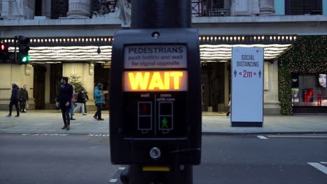 Eine-Von-Links-Nach-Rechts-Fahrende-LKW-Kamera-Fährt-An-Einem-Fußgängerüberwegsignal-Vorbei-Und-Zeigt-Menschen,-Die-An-Einem-Social-Distancing-Schild-Vor-Dem-Eingang-Des-Selfridges-Ladens-In-Der-Oxford-Street-Vorbeigehen