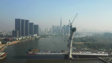 Drone-view-of-Saigon-River,-Ho-Chi-Minh-City-and-new-Thu-Thiem-Bridge-under-construction-on-a-sunny-day