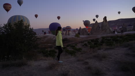 Frau,-Die-Bei-Sonnenaufgang-Einen-Bergrücken-In-Kappadokien-Hinaufgeht,-Um-Den-Start-Von-Heißluftballons-Zu-Beobachten