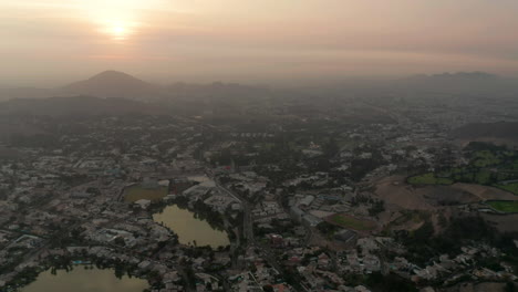 Aerial-track-shot-of-the-sun-setting-over-the-city-of-Lima-Peru,-showing-the-golden-haze-over-the-city
