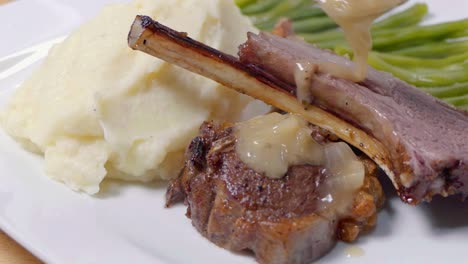 Slider-Shot-of-Adding-Sauce-to-Lamb-Cutlets-on-a-White-Plate-with-Mashed-Potato-and-Green-Beans