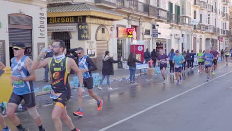 Exhausted-and-tired-marathon-runners-passing-water-dispensing-point-in-city-center-of-Malaga,-Spain