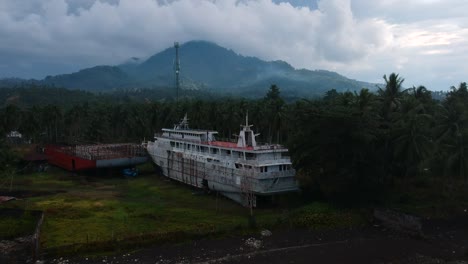 Aerial-drone-view-of-an-abandoned-cruise-shipwreck-on-an-isolated-tropical-island-with-a-dormant-volcano-in-the-foreground