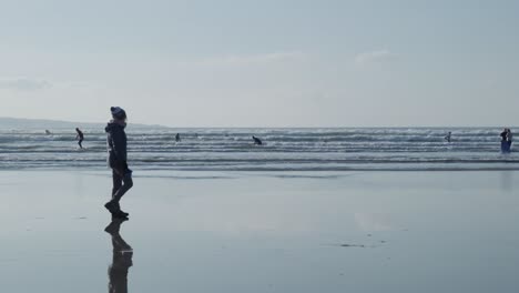 A-walker-strolls-by-as-surfers-ride-and-stand-in-the-water-in-this-perfect-slow-motion-shot