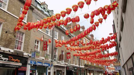 Red-Chinese-lanterns-swaying-in-summer-breeze-in-China-Town,-London-with-oriental-Asian-restaurants-and-shops