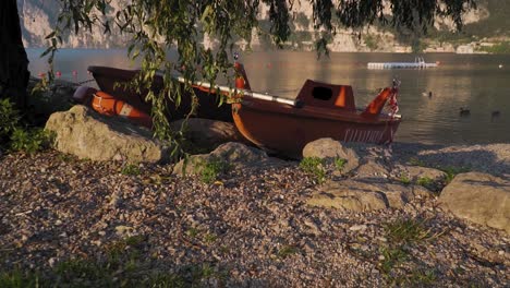 Old-boat-abandoned-at-lake-shore,-morning-lakeside-scenery,-golden-sunlight