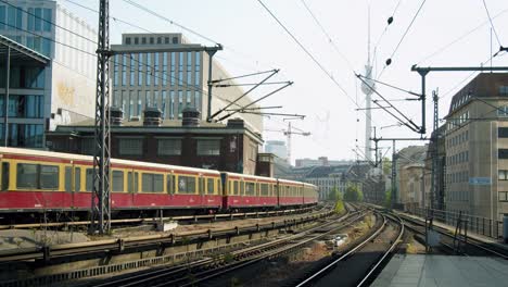 Berliner-U-Bahn-Fährt-An-Einem-Sonnigen-Tag-Am-Bahnhof-Vorbei,-Mit-Fernsehturm-Im-Hintergrund