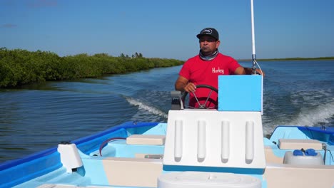 Medium-shot,-man-in-red-shirt-steering-the-boat-steering-wheel-on-the-sea-of-Adolfo-Lopez-Mateos-Baja-California-sur,-Mexico,-Scenic-view-mangrove-forest-in-the-background