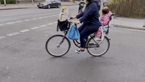 Slow-motion-shot-of-woman-riding-bike-with-dog-sitting-in-basket-in-front-and-child-in-baby-seat-in-back