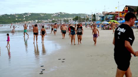 Dolly-in-of-people-walking-in-the-sand-near-the-seashore-in-the-area-of-Bombas-and-Bombinhas-beaches,-Brazil