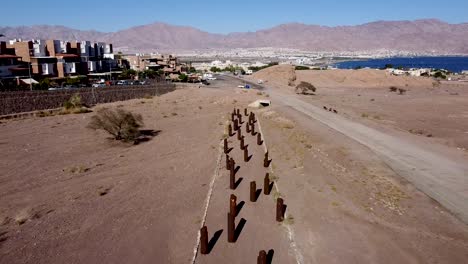 Aerial-slow-backwards-drone-shot-of-environmental-sculptures-lined-in-rows-near-the-city-of-Eilat,-surrounded-by-desert,-sea,-and-the-city