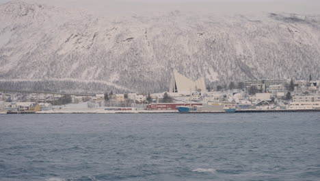 Wide-shot-showing-calm-water-of-fiord-and-snow-covered-mountains-and-famous-arctic-cathedral-in-background