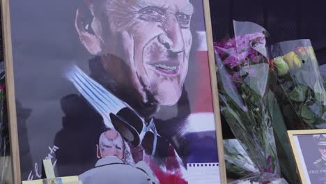 Buckingham-Palace-close-up-of-crowd-reflected-in-a-painting,-with-flowers-and-notes,-left-by-mourners-to-mark-the-death-of-Prince-Philip,-Duke-of-Edinburgh,-Saturday-April-10th,-2021---London-UK