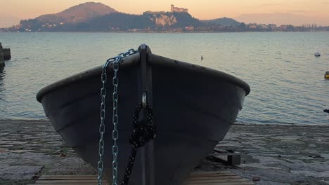 Fishing-boat-aground-and-tied-with-iron-chain-facing-Lake-Maggiore-and-Angera-castle,-Arona,-Italy