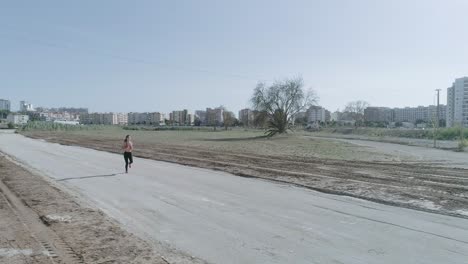 Rotating-drone-wide-shot-of-young-brunette-fitness-woman-running-on-urban-park-diet-road