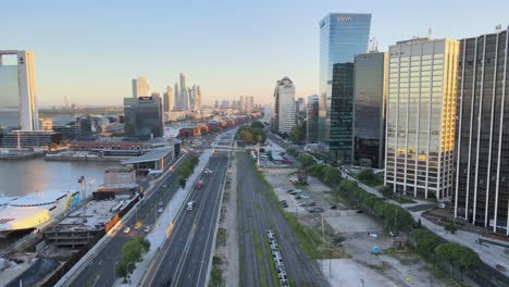 Aerial-dolly-in-of-Paseo-del-Bajo-highway-between-Puerto-Madero-docks-and-skyscrapers-at-sunset,-Buenos-Aires