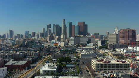 Rising-Crane-Shot-of-the-Downtown-Los-Angeles-Skyline-on-a-bright-day-with-cars-moving-California,-USA