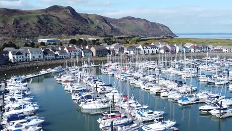 Luxury-yachts-and-sailboats-moored-in-Conwy-marina-mountain-waterfront-aerial-view-North-Wales-right-tilt-up