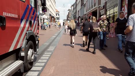 Side-view-of-fire-truck-moving-through-crowd-of-people,-pedestrian-zone-Nijmegen