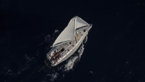 Top-Down-to-70---80-degree-tilted-slow-tracking-shot-of-monohull-sail-boat-moving-around-while-sailing-in-dark-blue-seas