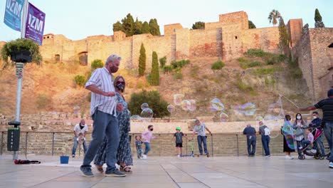 Guy-Wearing-Mask-Playing-Bubbles-With-Children-In-Front-Of-The-Ancient-Roman-Theatre-In-Malaga,-Spain---ground-level,-static-shot
