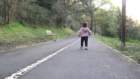 Back-view-of-toddler-running-on-asphalt-trail-in-park