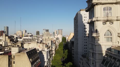 Aerial-dolly-out-revealing-Barolo-Palace-Tower-in-Avenida-de-Mayo-with-trees-surrounded-by-Buenos-Aires-buildings-at-sunset