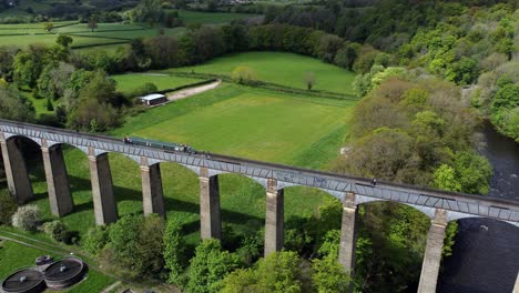 Aerial-view-following-narrow-boat-on-Trevor-basin-Pontcysyllte-aqueduct-crossing-in-Welsh-valley-countryside-rising-pull-back