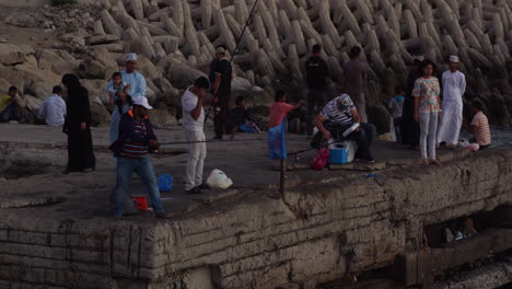 A-medium-group-of-people-fishing-in-a-dock-at-dusk-in-Muscat,-Oman,-wide-shot