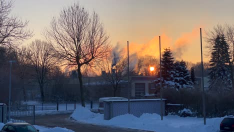 Rauch-Aus-Der-Fabrik-Und-Parkplatz-Voller-Schnee-Mit-Wunderschönem-Sonnenuntergang-Im-Hintergrund
