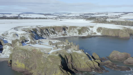 Aerial-view-of-Dunnottar-Castle-ruins-surrounded-by-snow-on-a-sunny-winter-day,-nr-Stonehaven,-Aberdeenshire,-Scotland